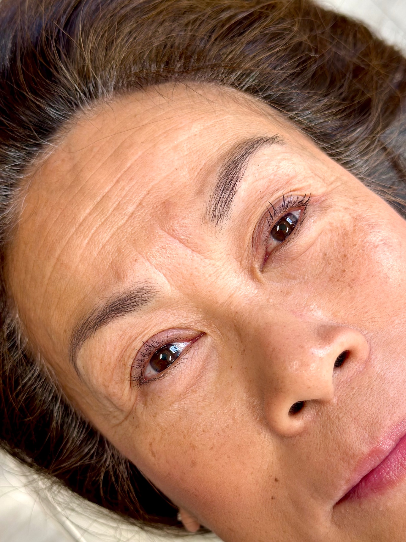 Healed nano brow result — client lying back with softly shaped brows
